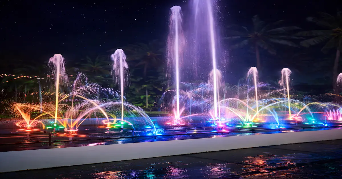 Colorful musical fountain show at night with illuminated water jets and palm trees in the background